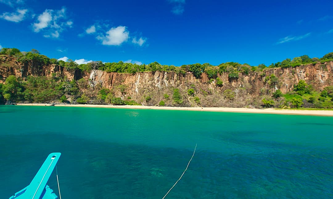 Barco chegando a praia entre falésias verdes de Fernando de Noronha